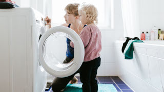 Junge Mutter mit einem Kind, das zusammen Kleidung wäscht